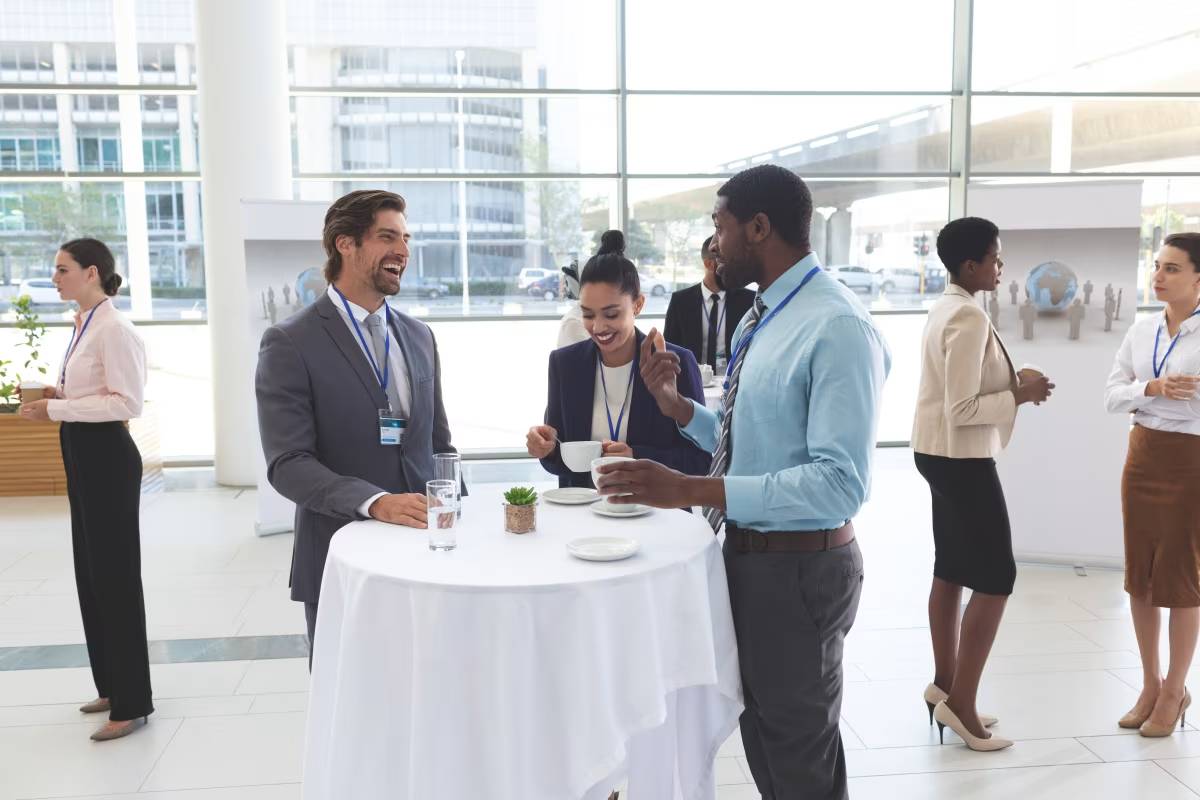 Group of professionals networking and conversing around a table at a business event, symbolizing event management and professional collaboration.